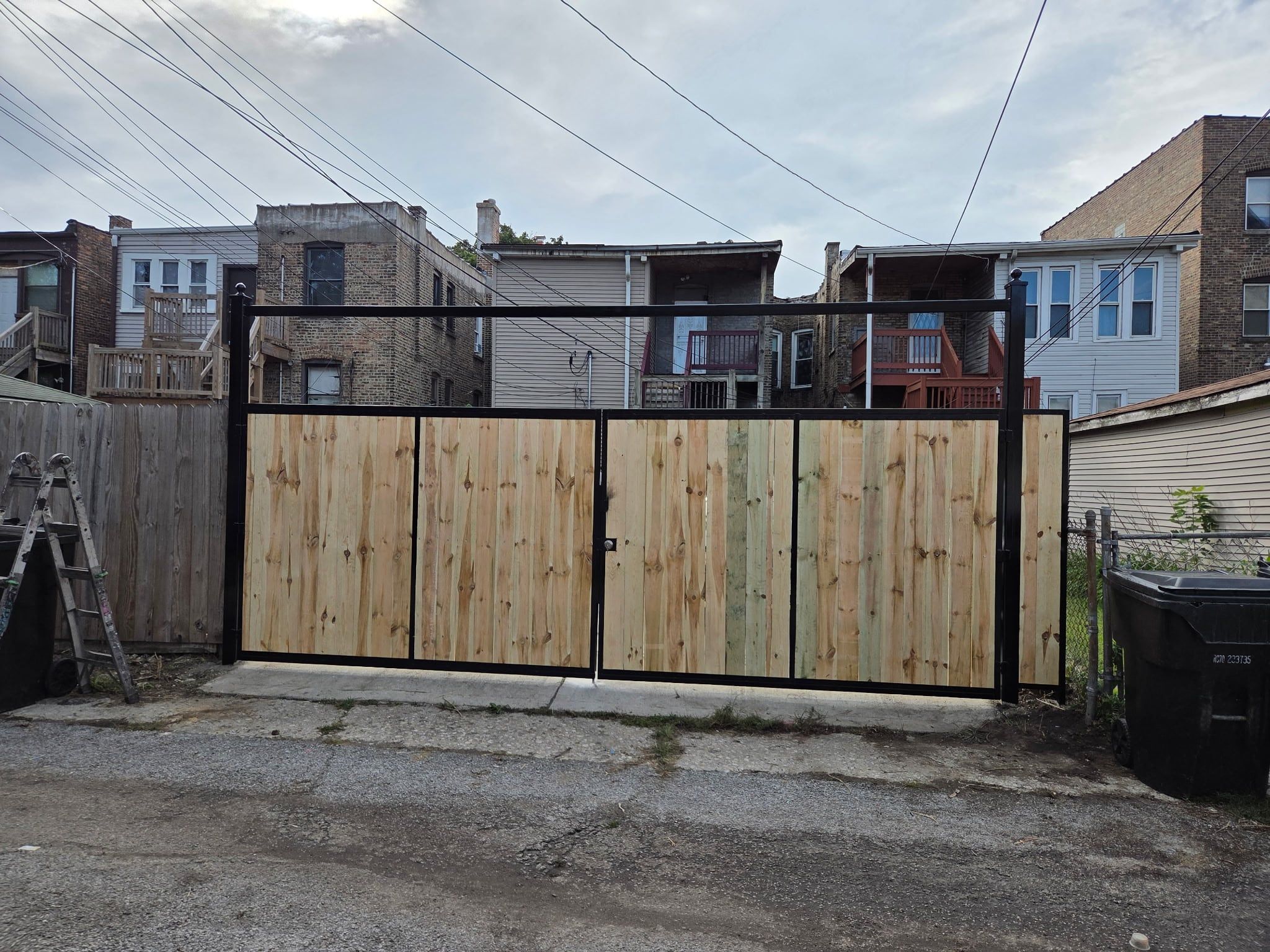 Finished double driveway gate with black steel frames and wood boards, closed, facing the alley