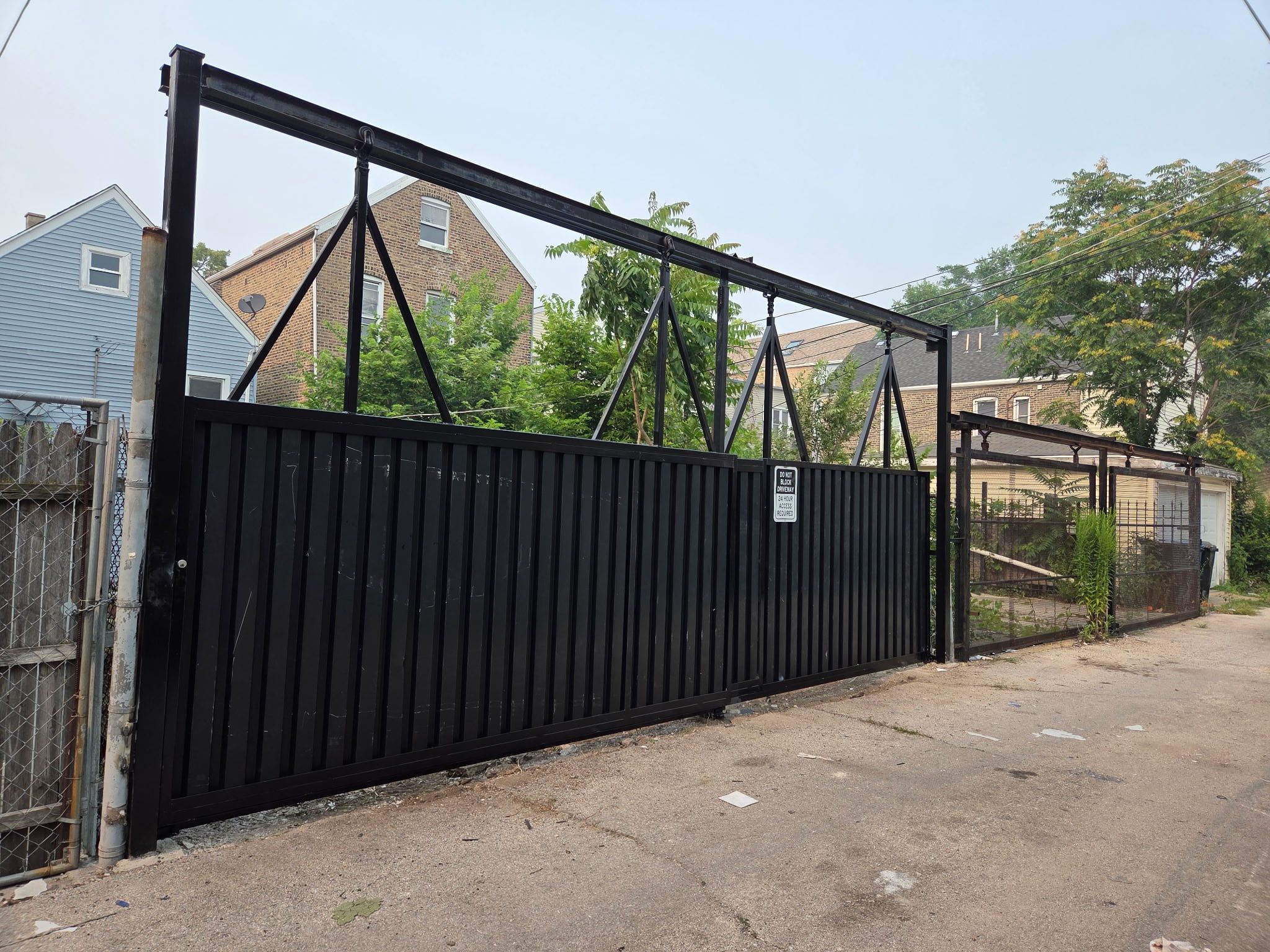 Black steel sliding driveway gate with an overhead steel frame facing the alley