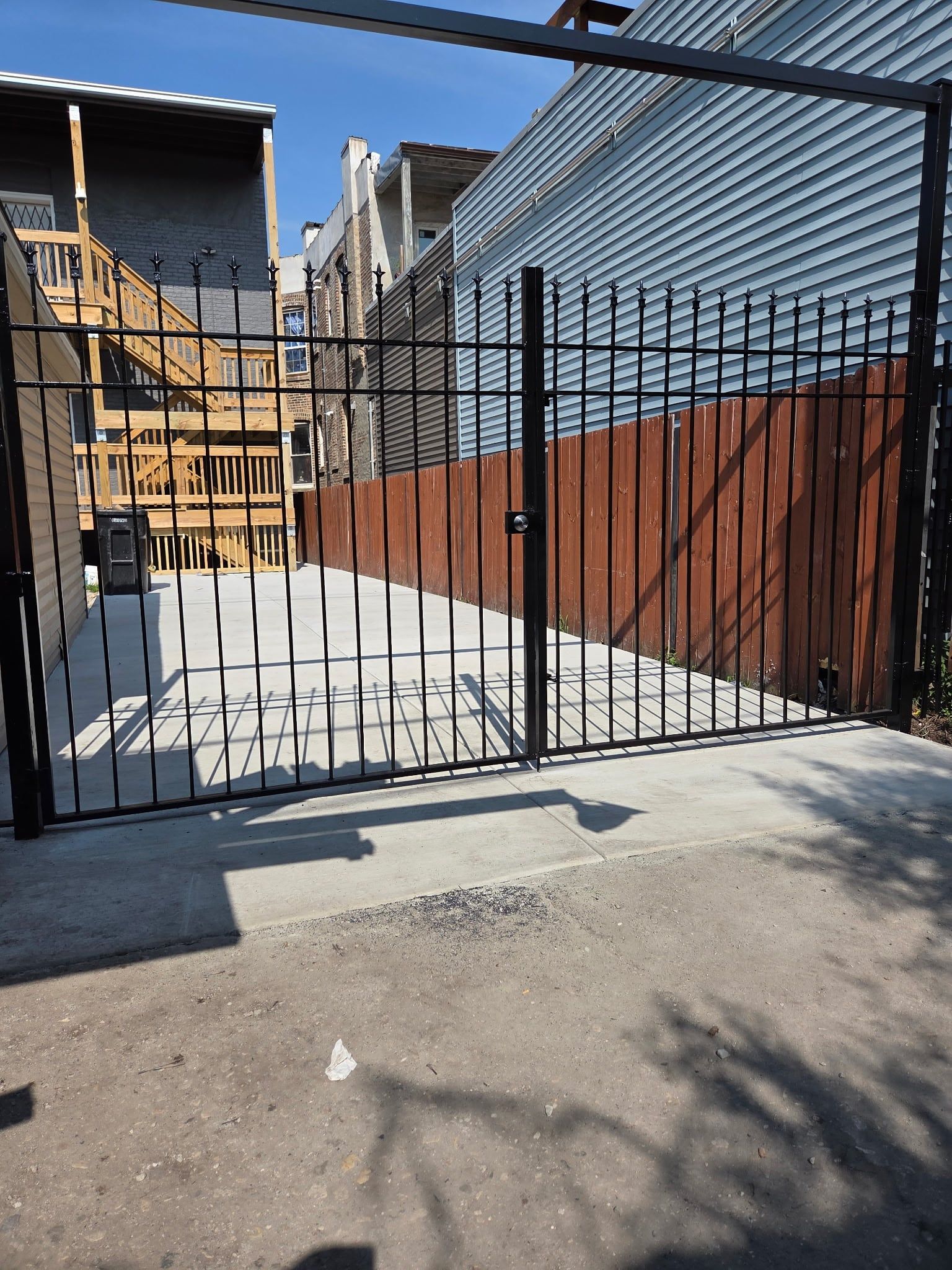 Black ornamental steel driveway gate with spear-top pickets beside a wood fence