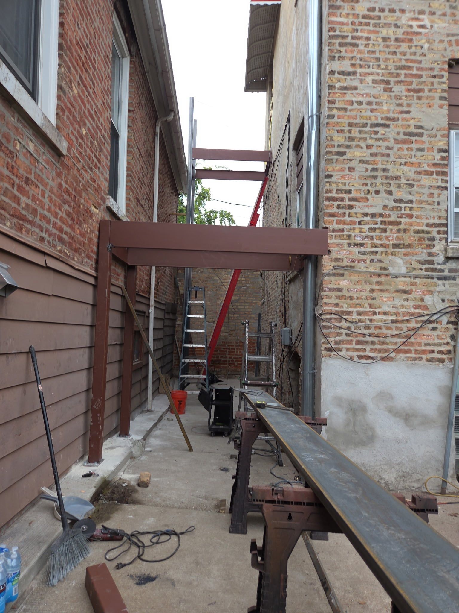 Primed steel stair frame going up in the gangway, with beams on sawhorses ready for welding