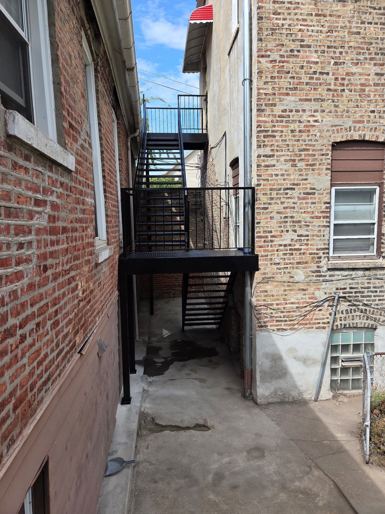 Finished black steel back stairs and landing rising two stories between brick buildings