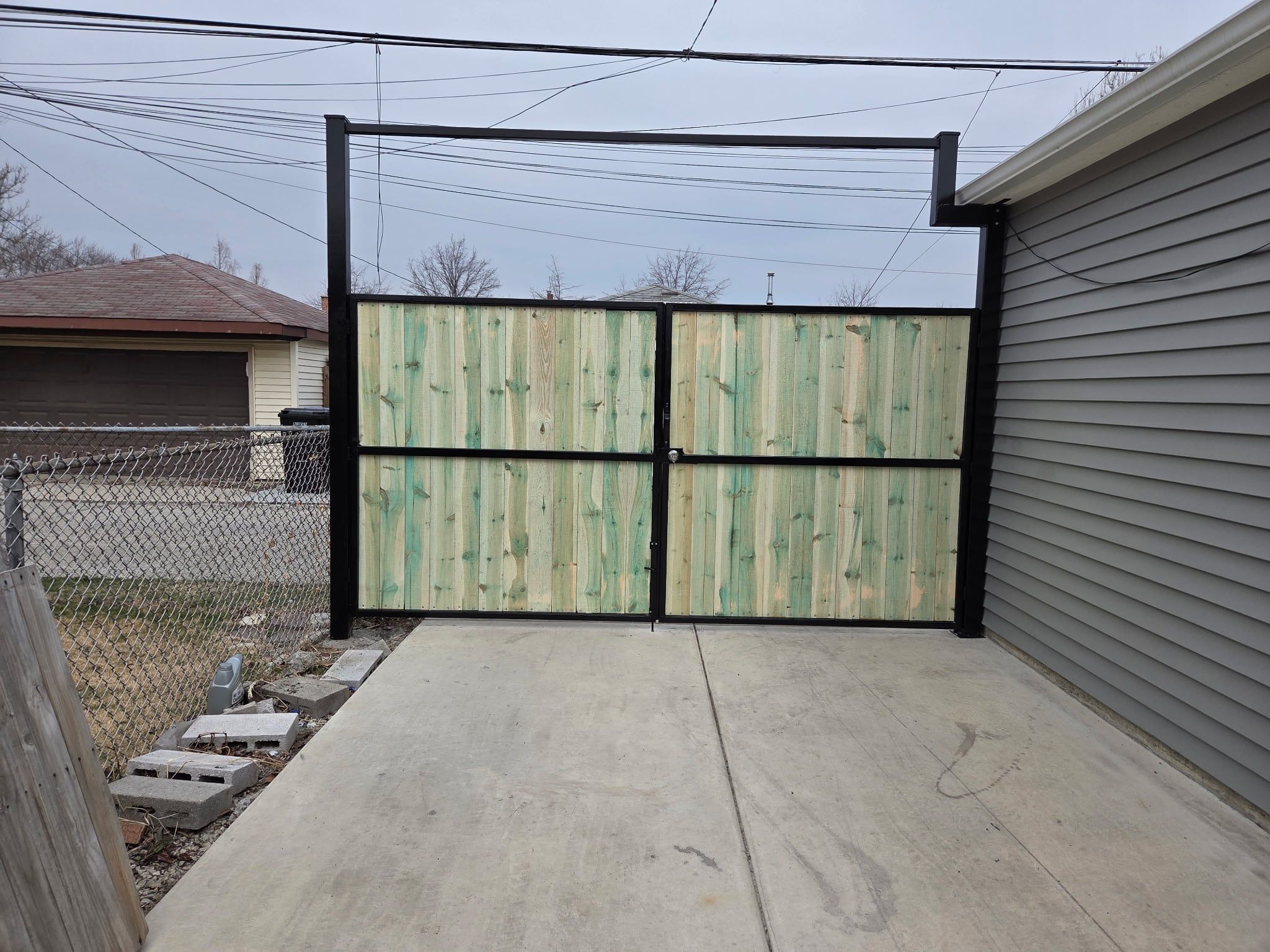 Closed double driveway gate with black steel frames and wood boards beside a garage