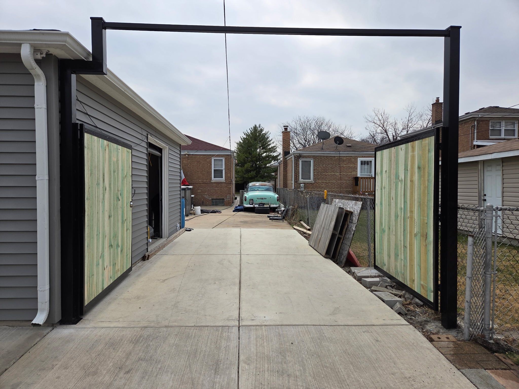 The same driveway gate standing open, showing the overhead steel header
